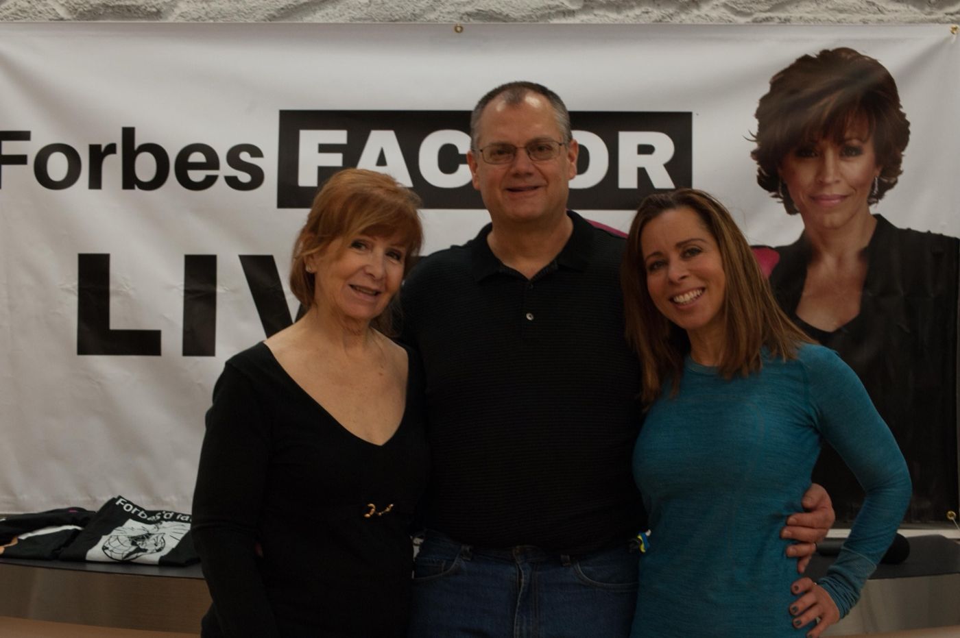 Three attendees in front of the Forbes Factor Live banner