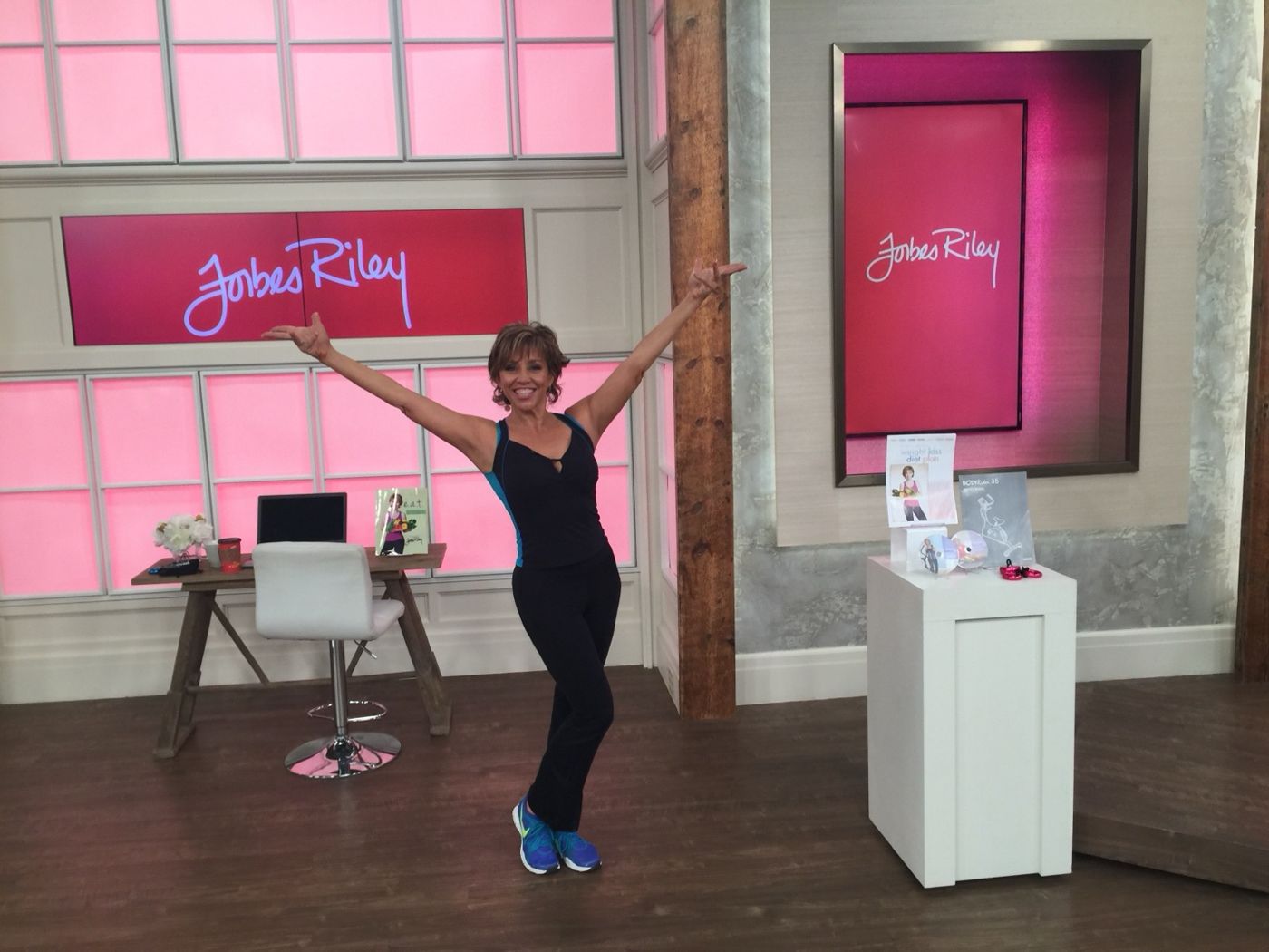 Forbes on her pink Forbes Riley television set, arms wide